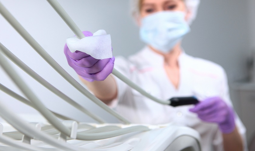 A nurse in uniform and wearing a medical mask wipes dental equipment. The face is out of focus. Gloved hand. Disinfection in the dental office. Copy of the space.